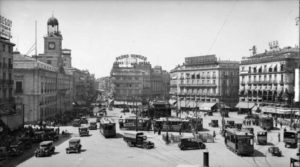 En el centro de la plaza vemos el templete, obra de Antonio Palacio, por el que se descendía al metro. Estuvo en ese lugar, tal y como podemos ver en la foto, hasta 1933, año en que fue retirado (aún se conservaría hasta 1970 el que existía en la Red de San Luis). En primer plano vemos los urinarios públicos (existían uno a cada lado de la plaza) y que permanecieron abiertos para el caminante con urgencias fisiológicas hasta la reforma de la plaza del año 1986, cuando los cerraron. 